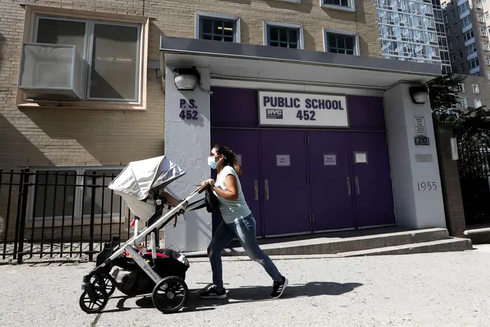 A woman pushes a baby stroller past Public School 452 in New York.